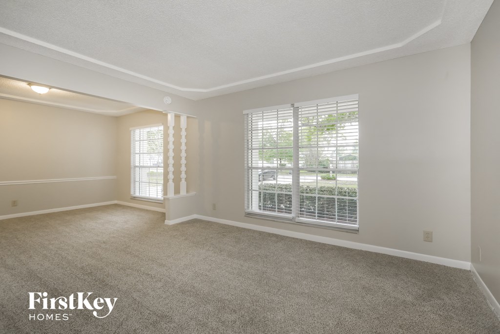 A spacious room with a carpeted floor and a window with blinds.