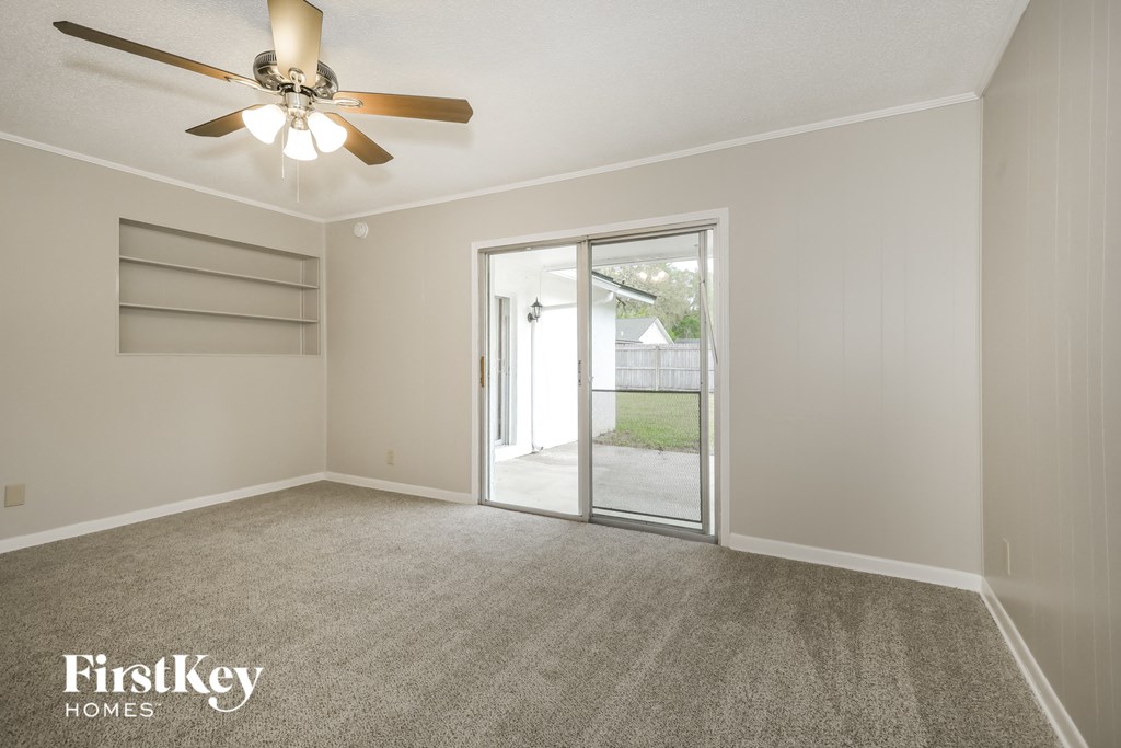 A spacious room with a ceiling fan and a sliding glass door leading to a patio.
