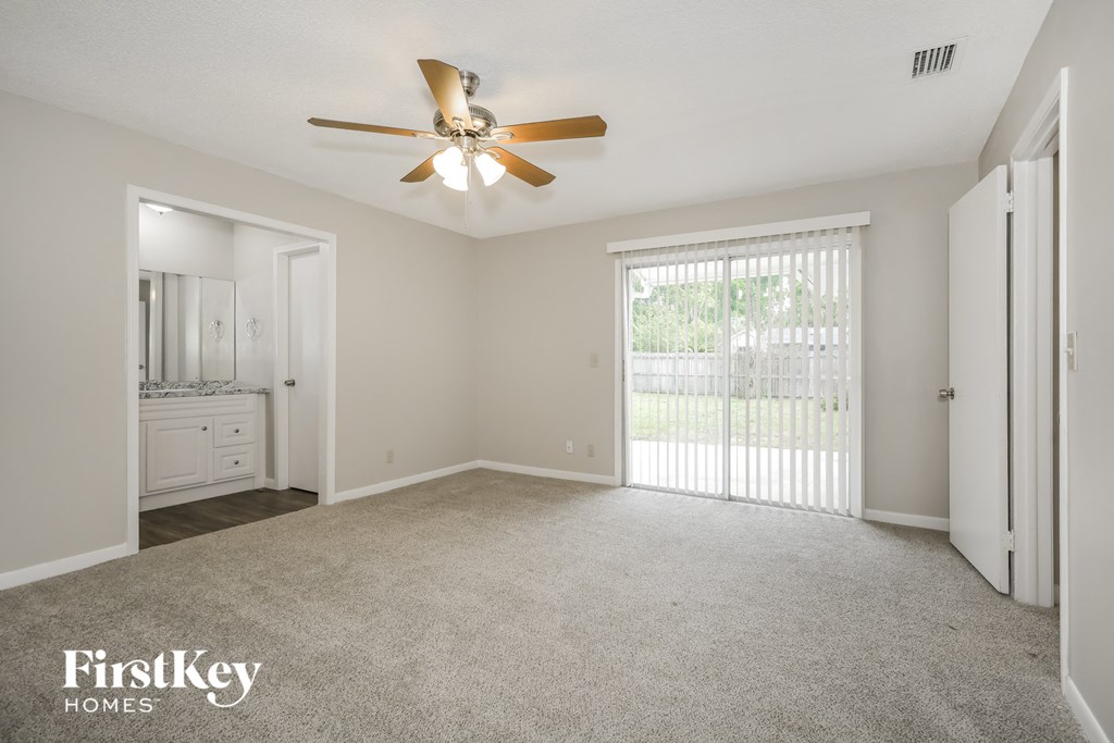 A spacious room with a ceiling fan and sliding glass doors leading to a balcony.