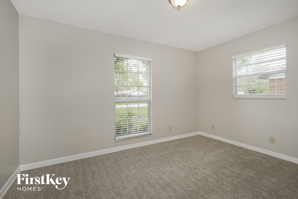A room with a carpet floor and two windows with blinds.