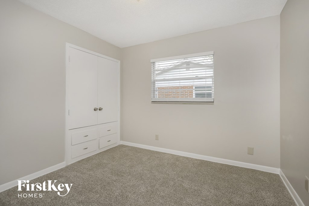 A bedroom with a white door, a window with blinds, and a carpeted floor.