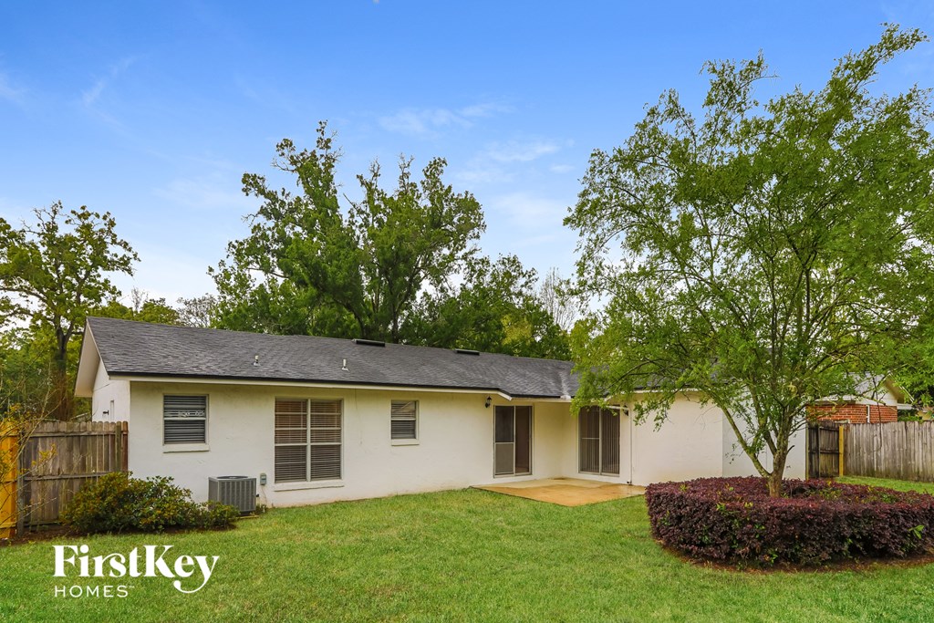 A white house with a brown fence and a tree in front.