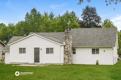 a small white house with a stone chimney on the side of a lawn