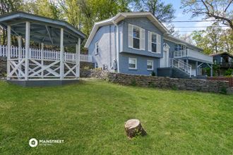 a blue house with a porch and a yard with a tree stump
