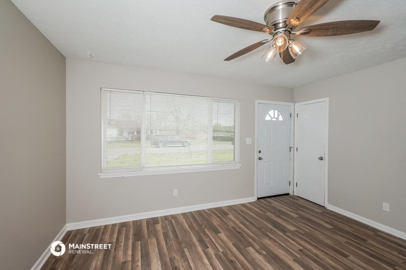the spacious living room with a large window and a ceiling fan