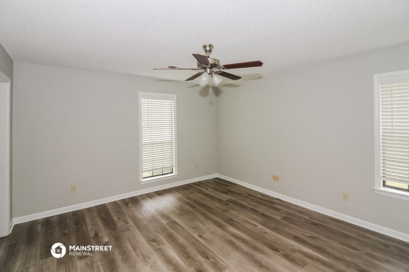 the spacious living room with wood flooring and a ceiling fan