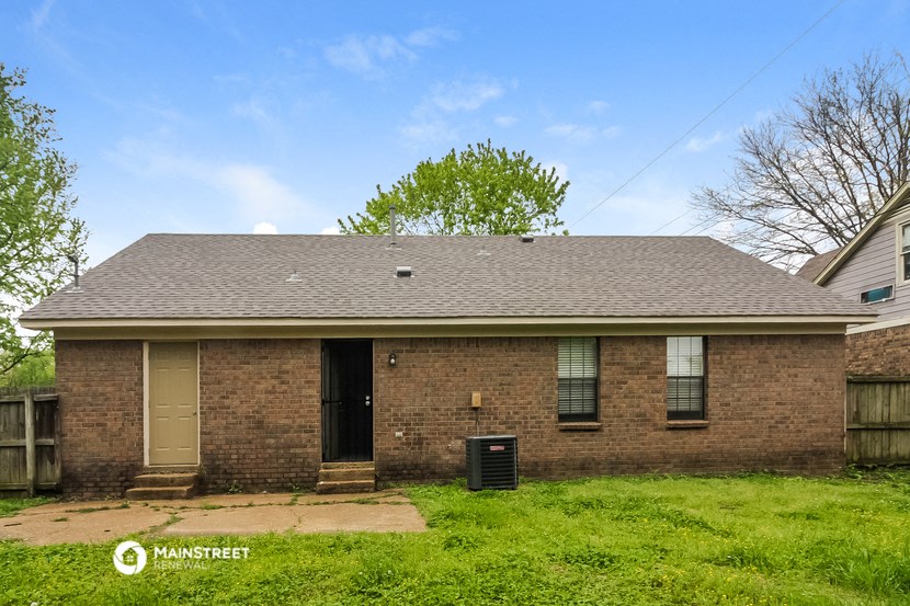 the front of a brick house with a yard and a trash can