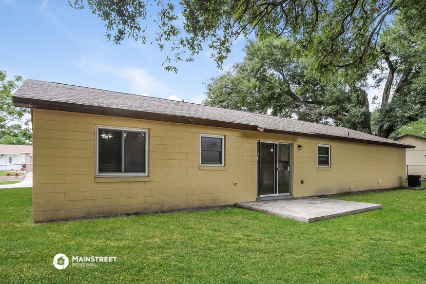 a small yellow brick house with a lawn and trees