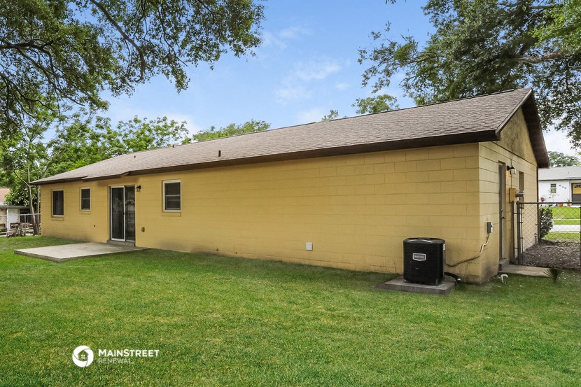 the backyard of a yellow house with a yard and a trash can