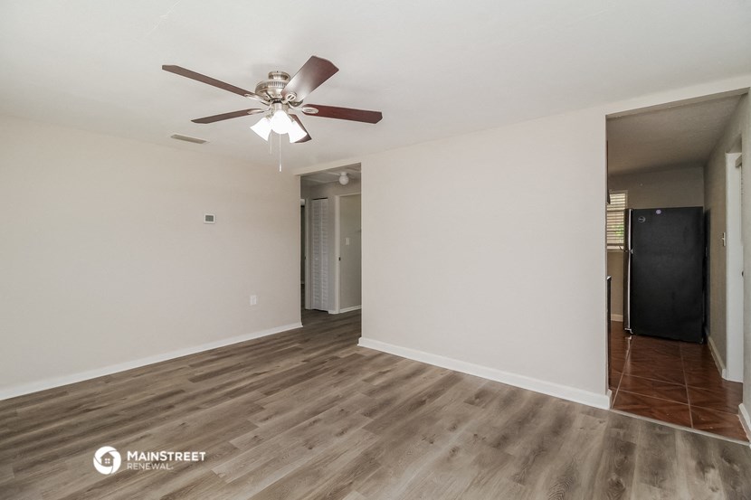 the living room of an apartment with white walls and a ceiling fan