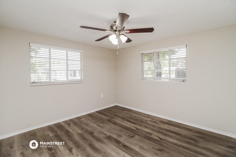 the spacious living room with wood flooring and a ceiling fan