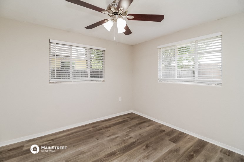 the spacious living room with wood floors and a ceiling fan