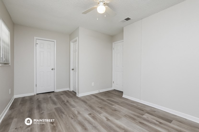 the spacious living room with white walls and a ceiling fan