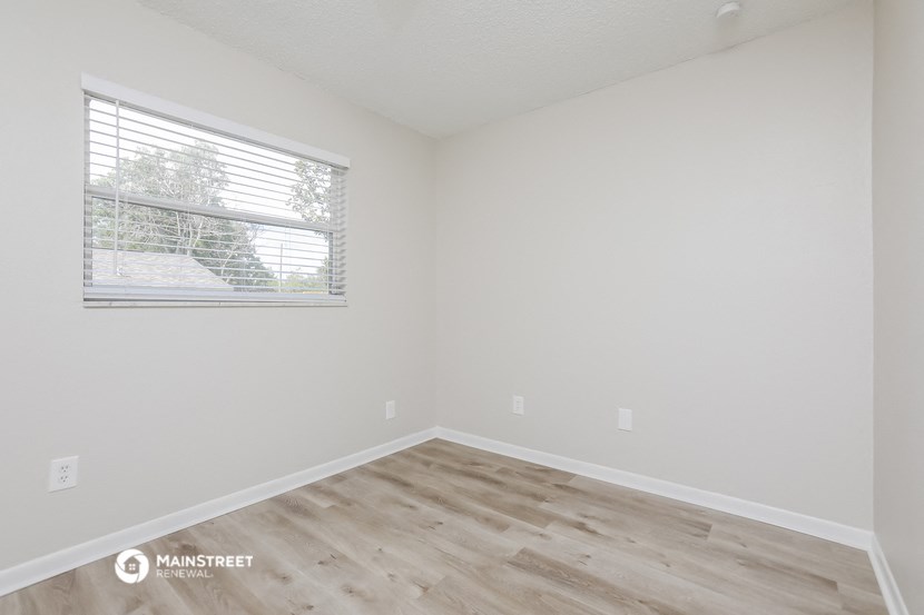 a bedroom with white walls and wood floors and a window