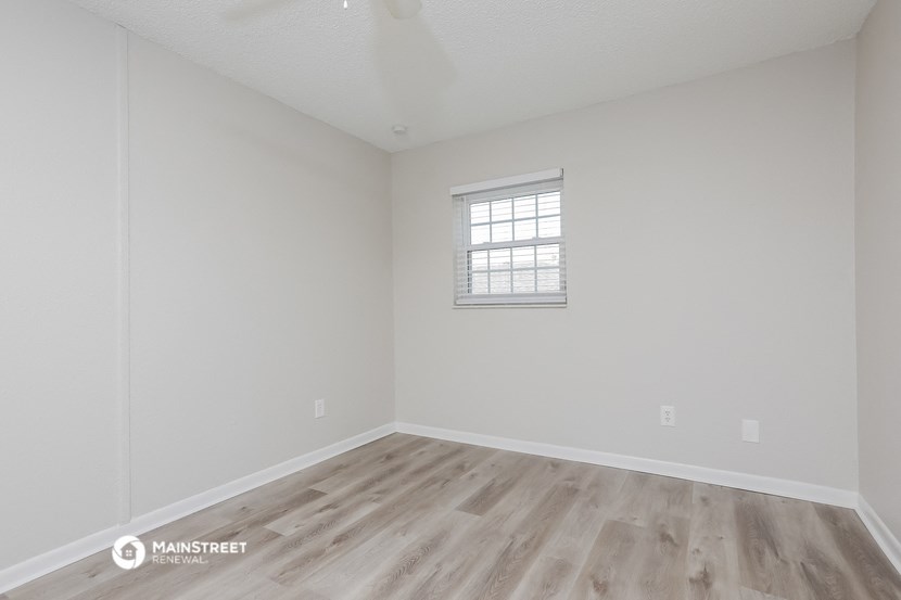 a bedroom with white walls and wood flooring and a window