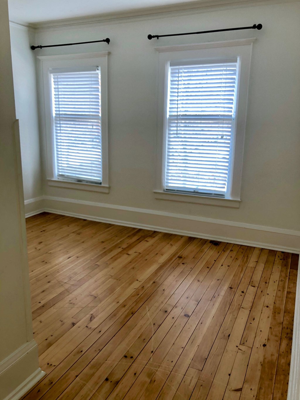 an empty room with wooden floors and two windows