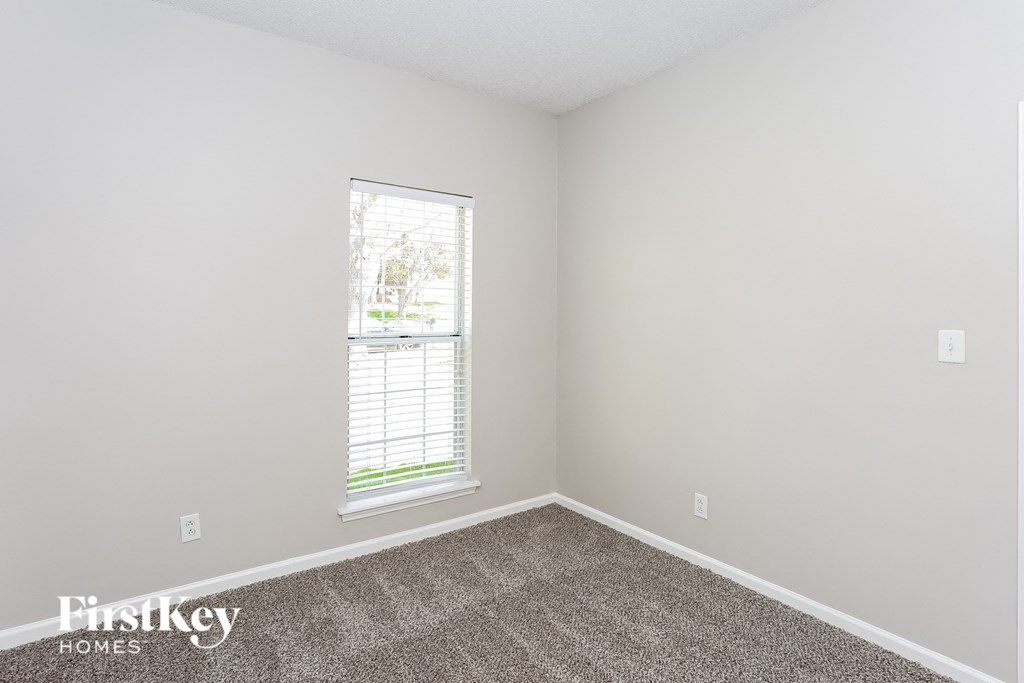 the bedroom of a small house with carpet and a window