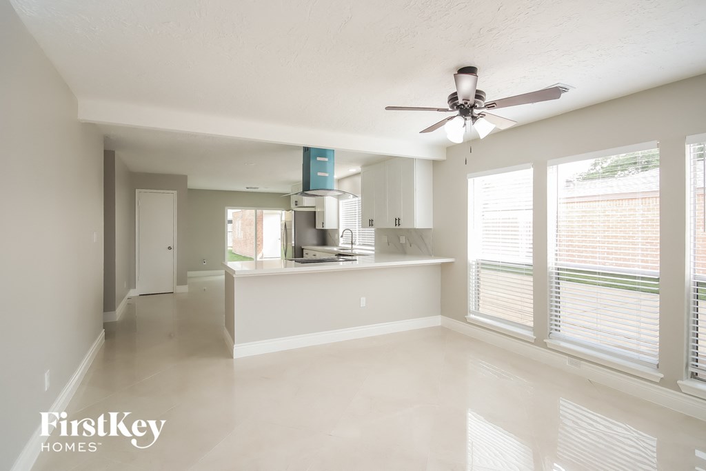A spacious, empty room with a ceiling fan and large windows.