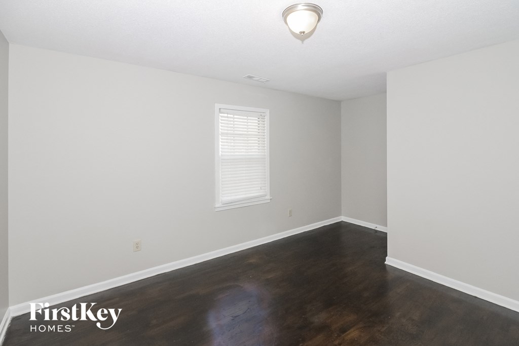 a bedroom with white walls and wood floors and a window