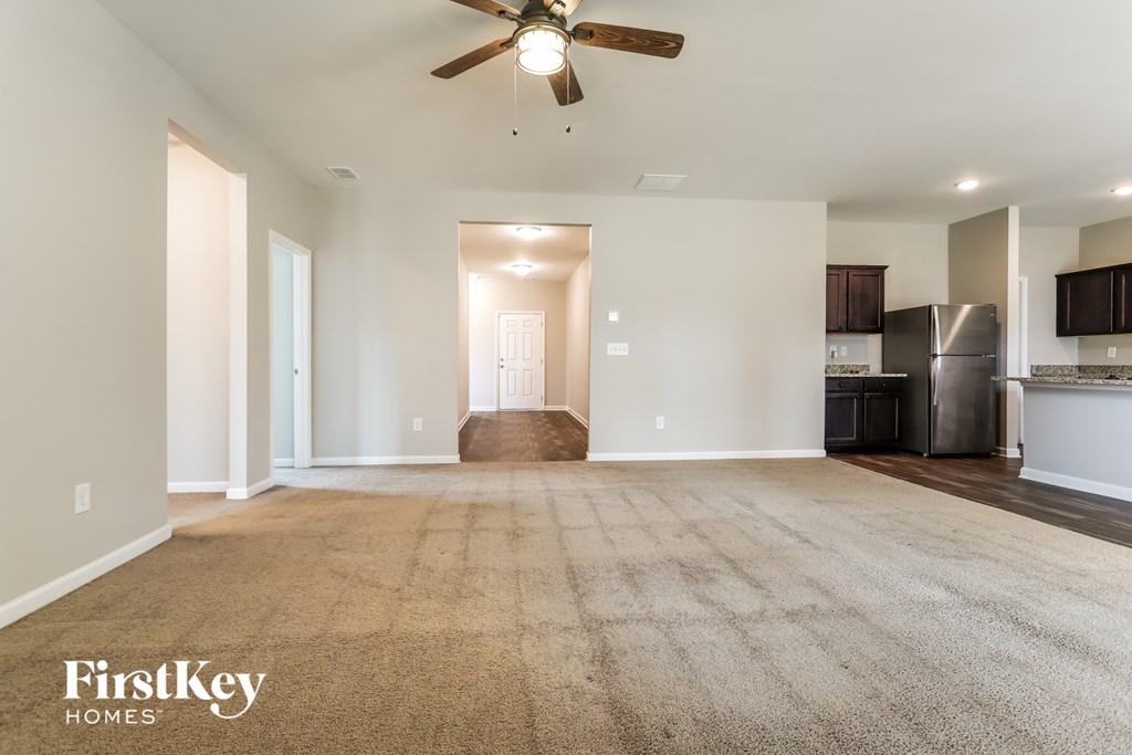 an empty living room with a ceiling fan and a kitchen