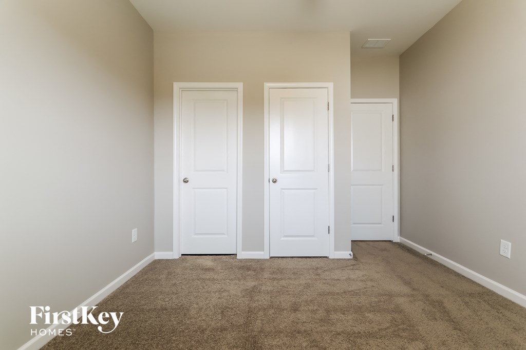 a carpeted room with two white doors and two closet doors