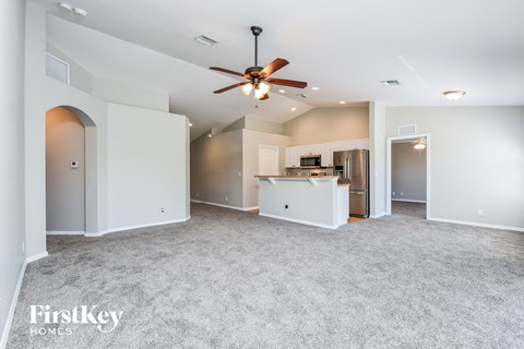 A spacious living room with a ceiling fan and a kitchen area in the background.
