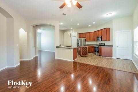 an empty living room and kitchen with wood flooring and a ceiling fan