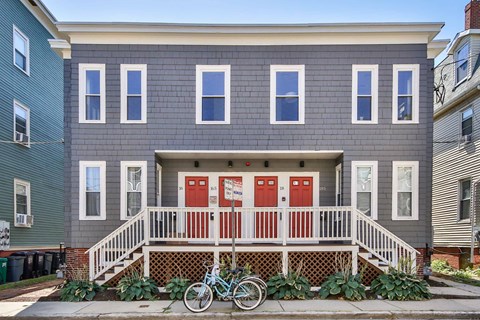A grey house with a red door and a bicycle in front.