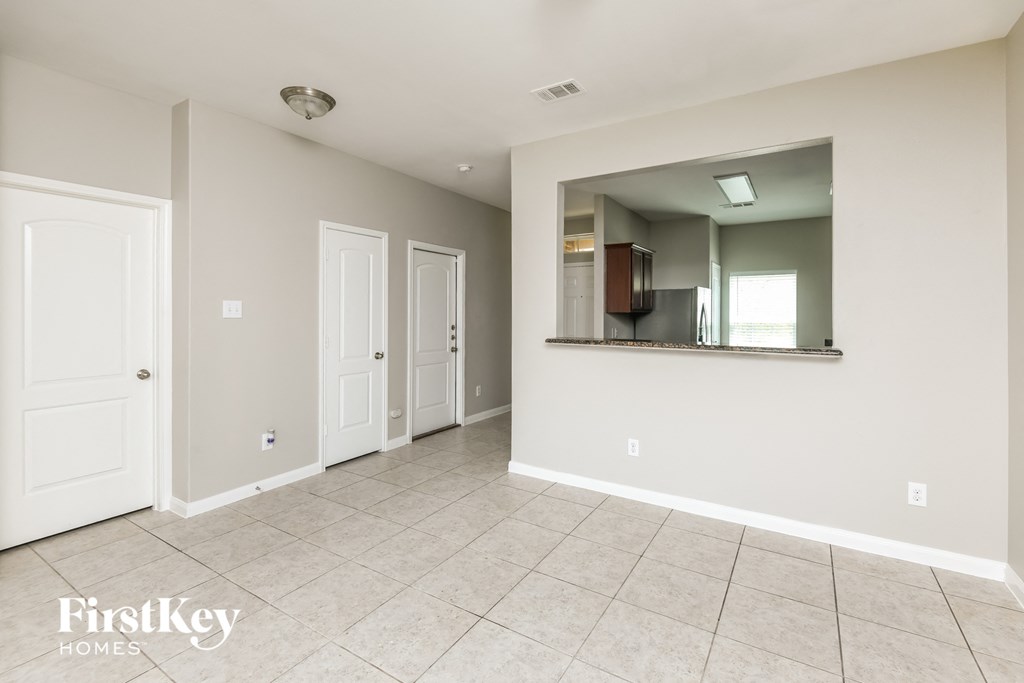 an empty living room with a mirror and a door to the kitchen