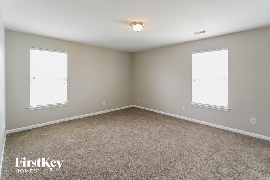 A room with a carpeted floor and two windows.