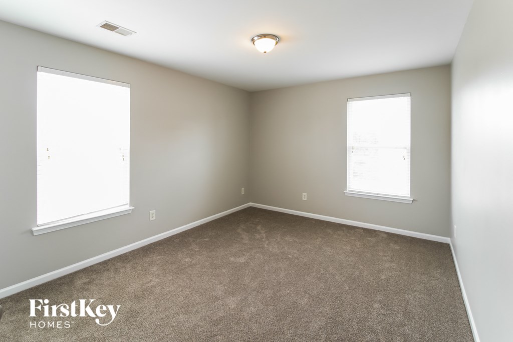 A room with a carpeted floor and two windows.