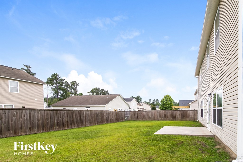 A backyard with a wooden fence and a house with the words "FirstKey Homes" on it.
