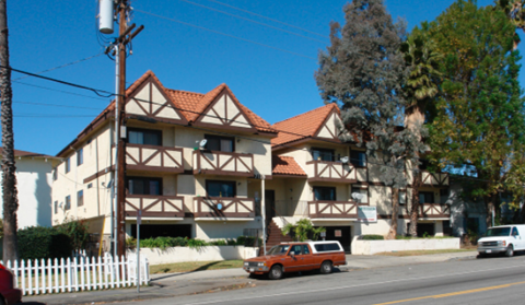 A white picket fence in front of a brown and white building.