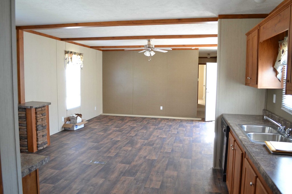 an empty living room with a kitchen and a ceiling fan