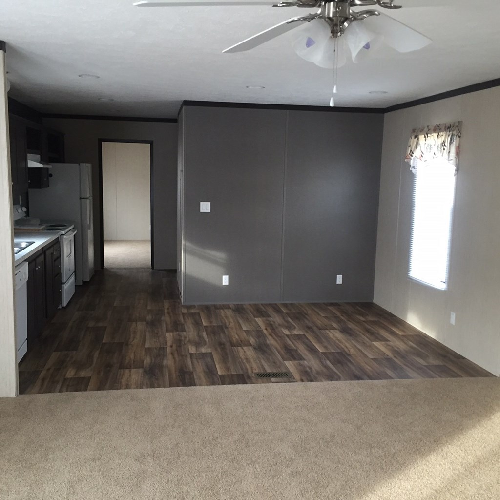 an empty living room with a kitchen and a ceiling fan