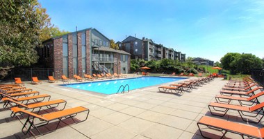 Huge swimming pool with spacious sundeck, poolside lounge chairs, beautiful landscaping, and scenic views at LionsHead Apartments in Omaha, Nebraska