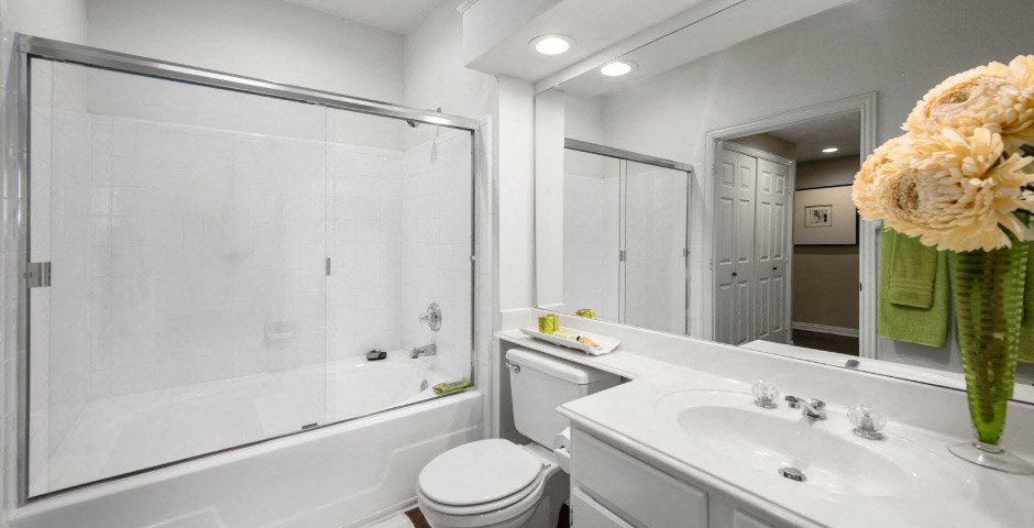 Spacious bathroom with oval soaking tub with glass enclosure, cultured marble vanity, glass shower, and built-in vanity at The Lanesborough Apartments in Houston.