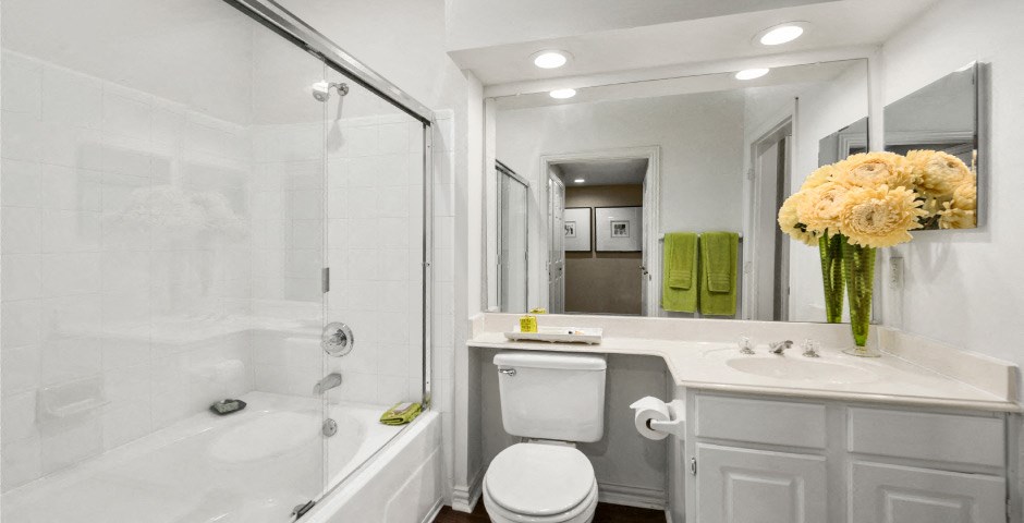 Spacious bathroom with oval soaking tub with glass enclosure, cultured marble vanity, glass shower, and built-in vanity at The Lanesborough Apartments in Houston.