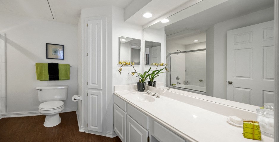 Spacious bathroom with oval soaking tub with glass enclosure, cultured marble vanity, glass shower, and built-in vanity at The Lanesborough Apartments in Houston.