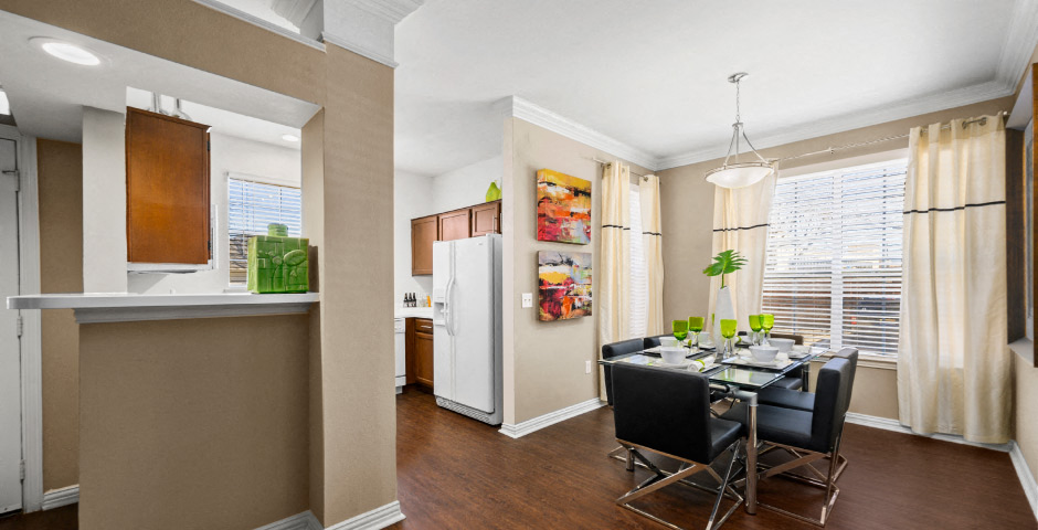 Spacious dining room with wood grain plank flooring, oversized windows, spacious kitchen with white appliances and side by-by-side refrigerators The Lanesborough Apartments in Houston.