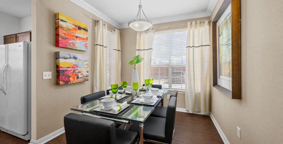 Spacious dining room with wood grain plank flooring, oversized windows, spacious kitchen with white appliances and side by-by-side refrigerators The Lanesborough Apartments in Houston.