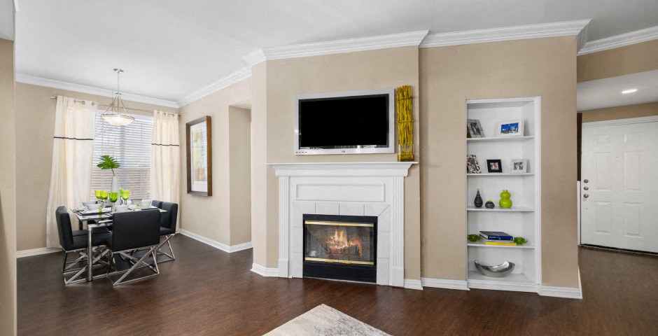 Spacious living room and dining room with wood-burning fireplace with glass doors, ceiling fan, 9-foot ceilings and wood grain plank flooring at The Lanesborough Apartments in Houston.