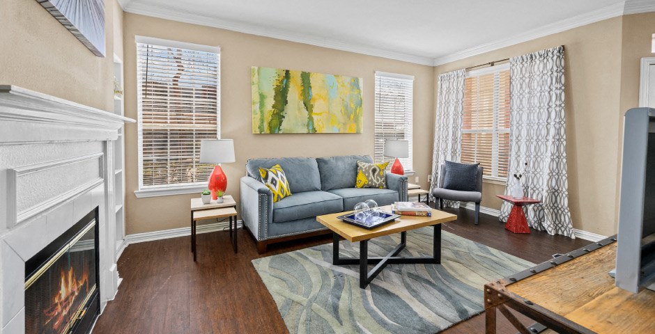 Spacious living room with wood-burning fireplace with glass doors, ceiling fan, 9-foot ceilings, built-in shelves and wood grain plank flooring at The Lanesborough Apartments in Houston.