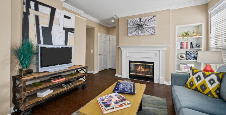 Spacious living room with wood-burning fireplace with glass doors, 9-foot ceilings, built-in shelves, and wood grain plank flooring at The Lanesborough Apartments in Houston.