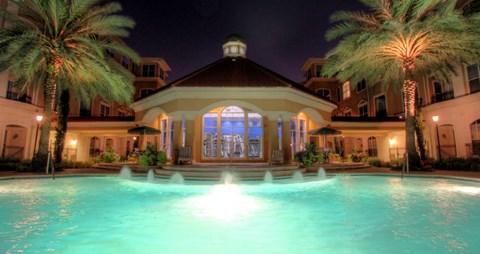 Resort-style pool with fountains, pool-side lounge chairs, and palm trees at Tuscany Court Apartments in Houston.