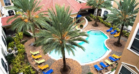 Luxury apartments with resort-style pool with fountains, pool-side lounge chairs, and palm trees at Tuscany Court Apartments in Houston.
