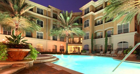 Resort-style pool with fountains, pool-side lounge chairs, and palm trees at Tuscany Court Apartments in Houston.