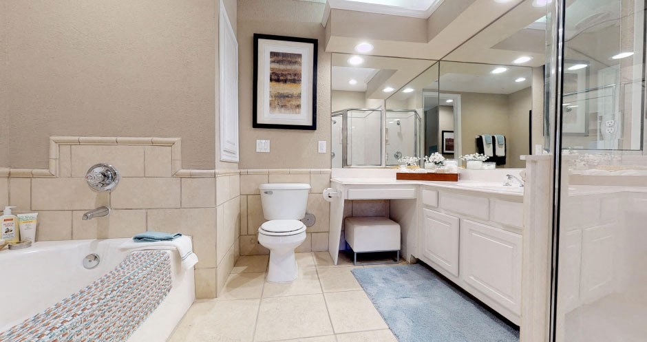 Spacious bathroom with oval soaking tub with glass enclosure, cultured marble vanity, glass shower, and built-in vanity at Tuscany Lane Apartments in Houston.
