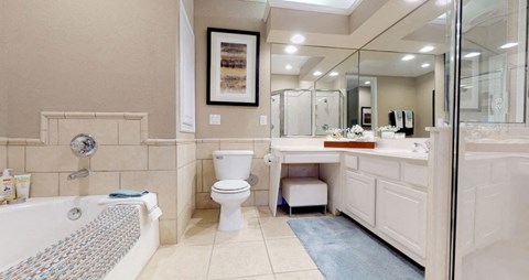 Spacious bathroom with oval soaking tub with glass enclosure, cultured marble vanity, glass shower, and built-in vanity at Tuscany Lane Apartments in Houston.