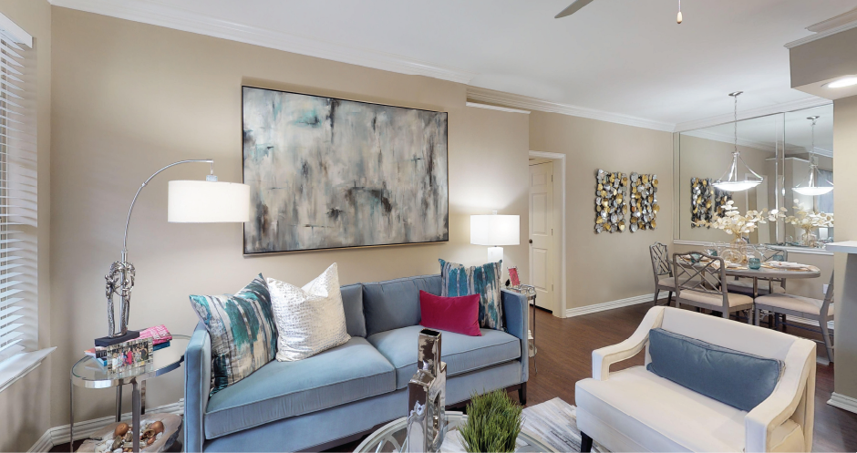 Spacious living room and dining room with mirror accent wall, hardwood floors, and breakfast bar at Tuscany Park Apartments in Houston.